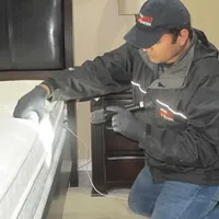 Bed bug inspection technician checking a mattress and bed frame for signs of infestation in Ogden, UT